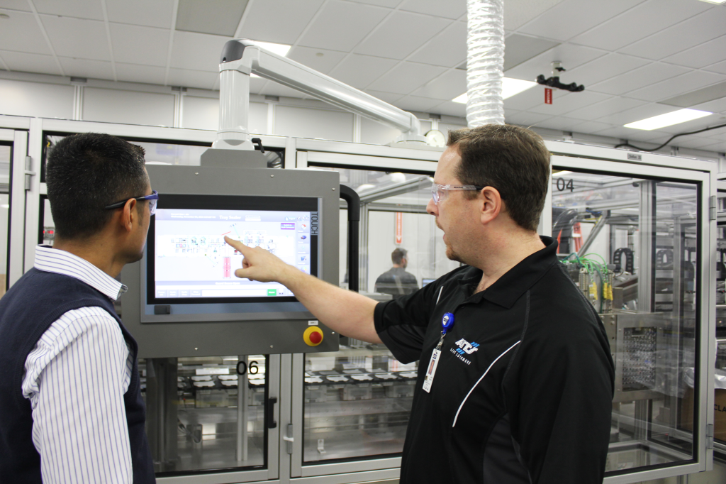 Two operators standing in front of an operator's screen on a machine, reviewing machine performance