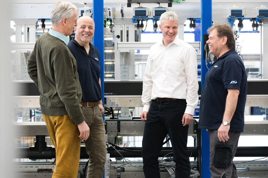 Vier männliche Kollegen stehen neben einer Maschine und genießen die gemeinsame ZeitGute
