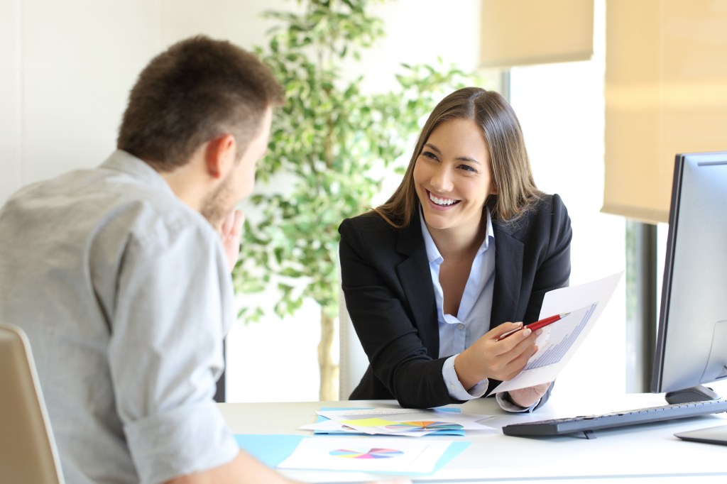 Ein männlicher und ein weiblicher Mitarbeiter besprechen die Arbeit an einem BesprechungstischMitarbeitervorteile